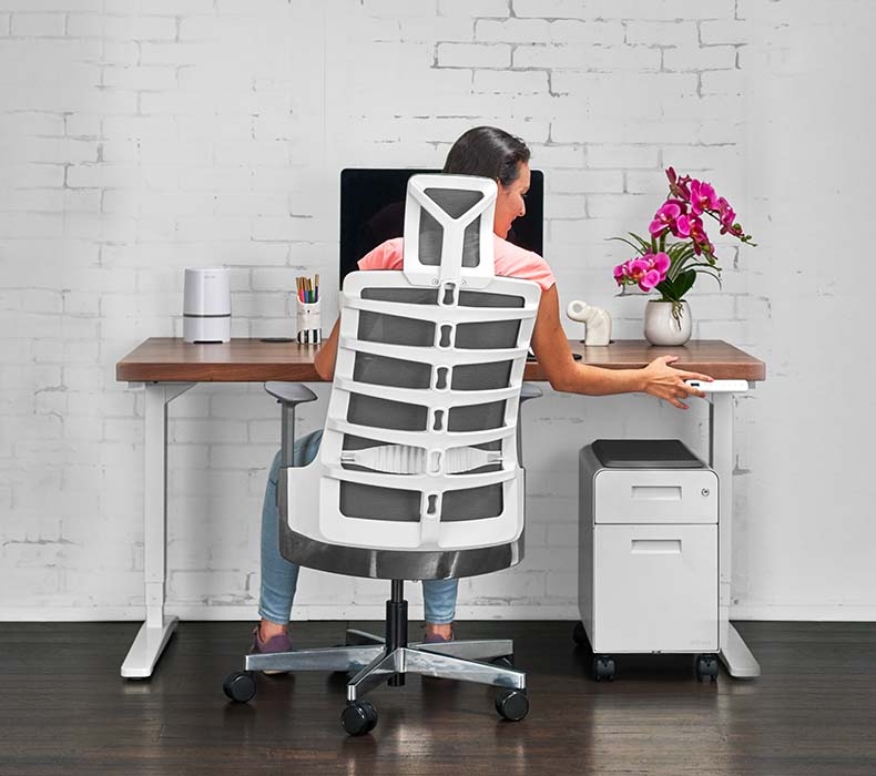 A woman seated in a computer chair while working at a standing desk by UPLIFT. 