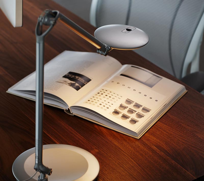 A Humanscale Element Disc LED Task Light illuminating a book on a desk