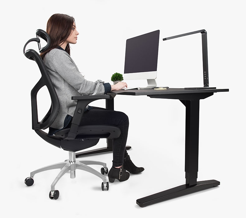 A woman sitting in a J3 Ergonomic Chair at a UPLIFT V2 Standing Desk