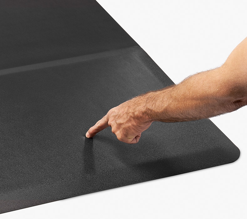 A finger pressing down on the padded section of the Chair Mat with Standing Cushion to show foam support