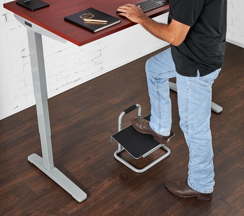 Resting one foot on the repositionable desk footrest