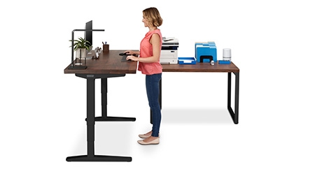 A person standing by an UPLIFT standing Desk and a fixed height UPLIFT table