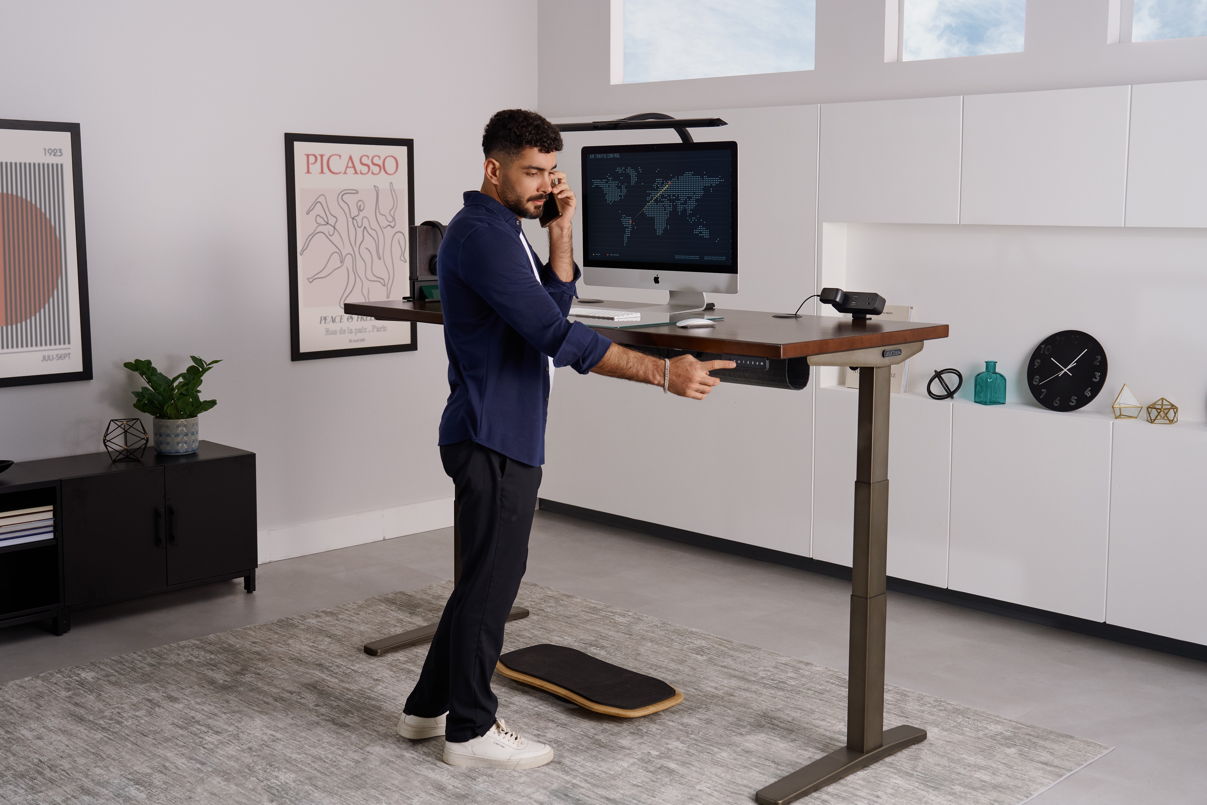 Person standing at an Uplift Desk and pressing a button on the keypad while on the phone