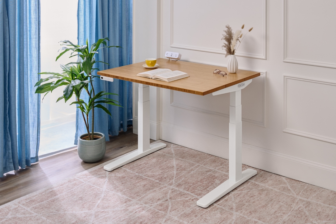 UPLIFT Desk 2-leg standing desk with a bamboo desktop in a student dorm setting.