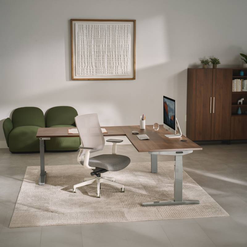 UPLIFT V3 L-Shaped Standing Desk with gray frame and laminate desktop in a small home office setting