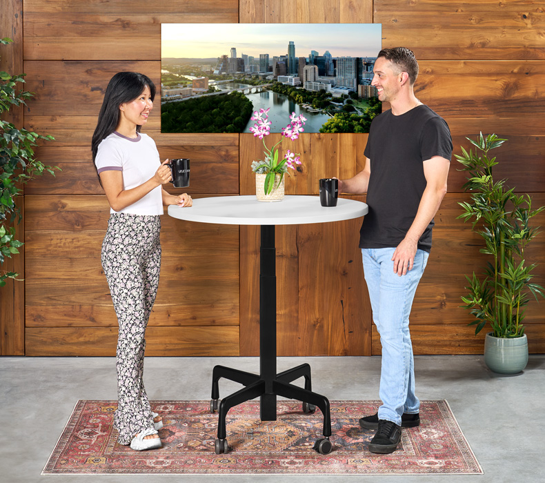 Two people on break having coffee while standing at an UPLIFT Height Adjustable Bistro Table