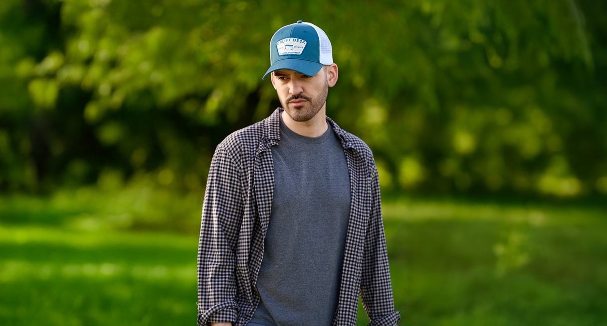 Man looking down while walking through nature, wearing an UPLIFT Desk Cap