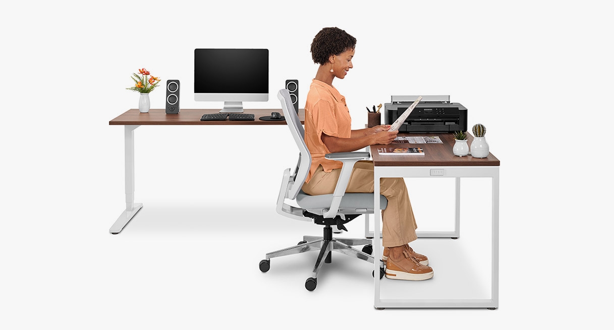 A person working at a Walnut Wide Plank Solid Wood O-Leg Seated Height Table