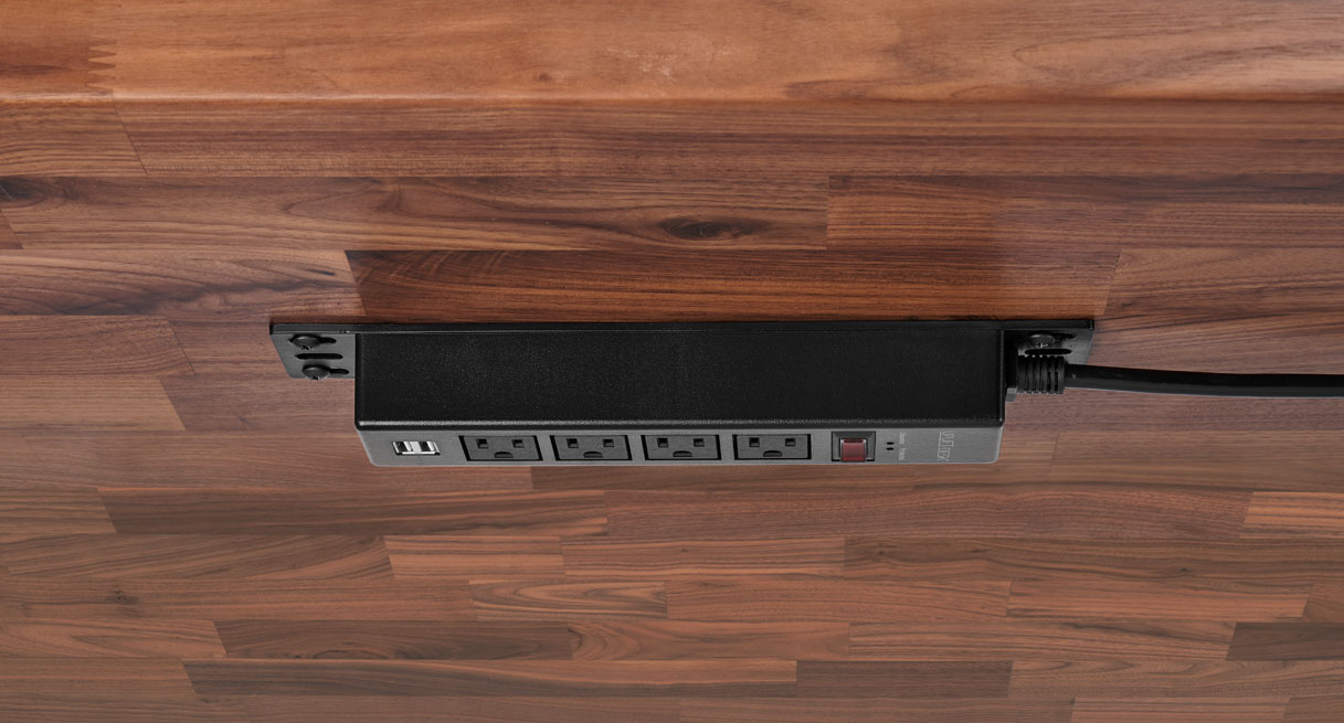 An outlet power strip attached directly to the underside of a desktop