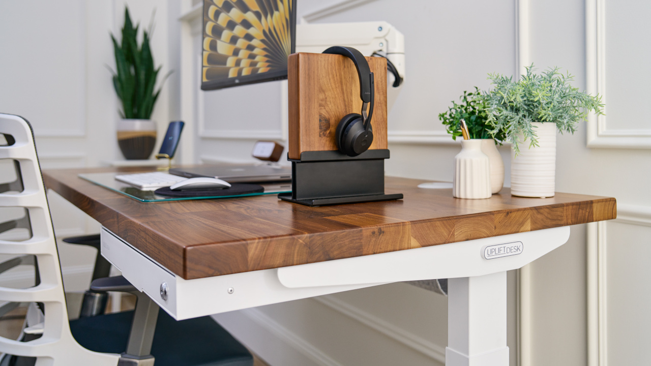 A walnut Headphone Stand sits on top of an Uplift Standing Desk with a walnut desktop to match.