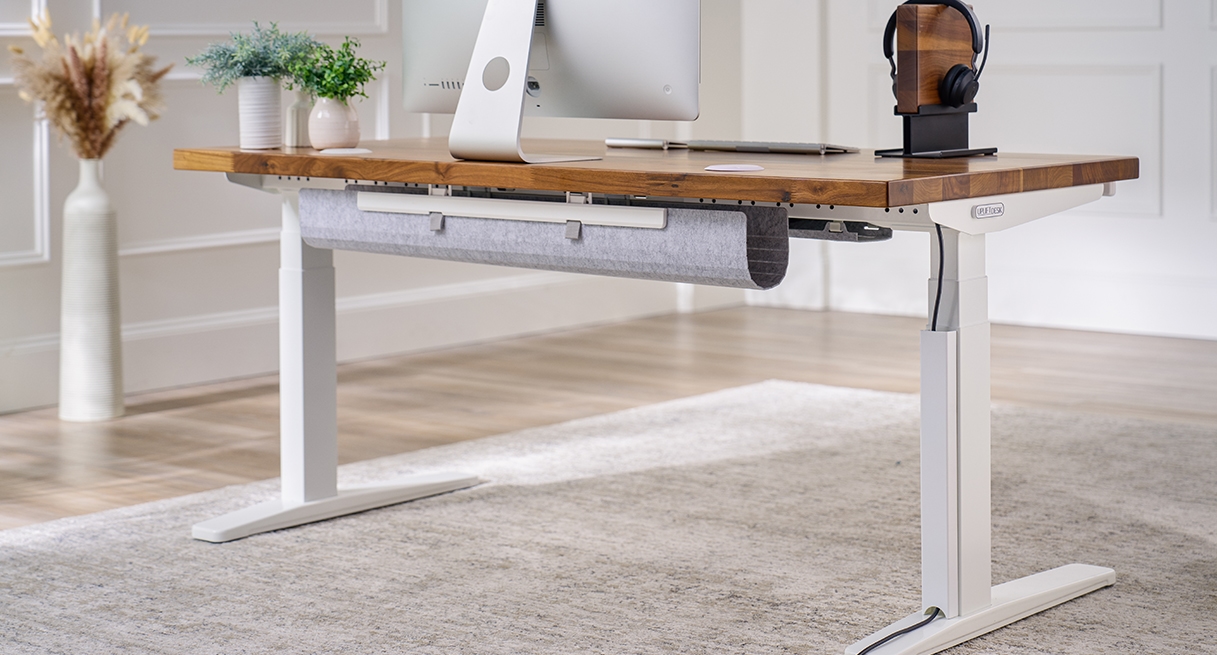 UPLIFT Magnetic Cable Channel shown organizing a cable under standing desk with white frame and solid wood desktop