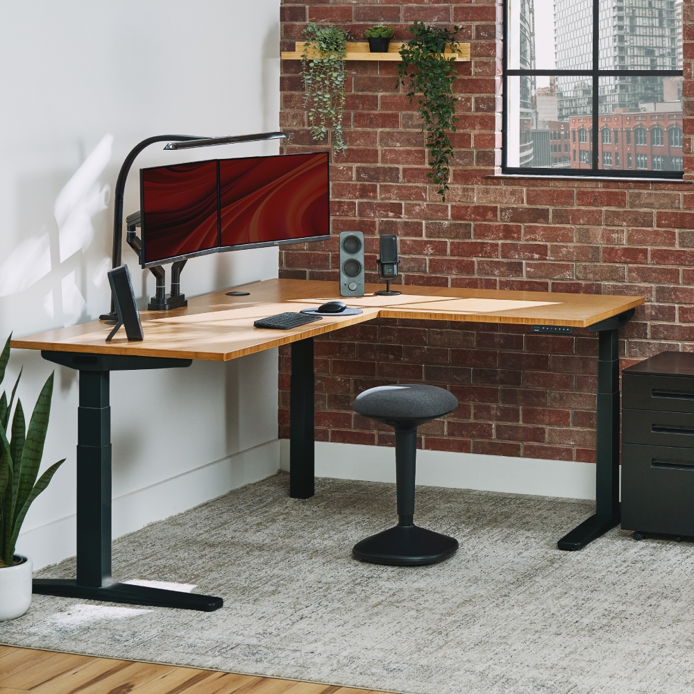 UPLIFT V3 L-Shaped Standing Desk with a bamboo desktop and black frame in a music production office.