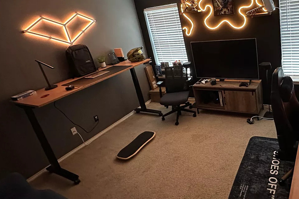 A cozy office space with neon lighting and gaming memorabilia featuring an Uplift Standing Desk.