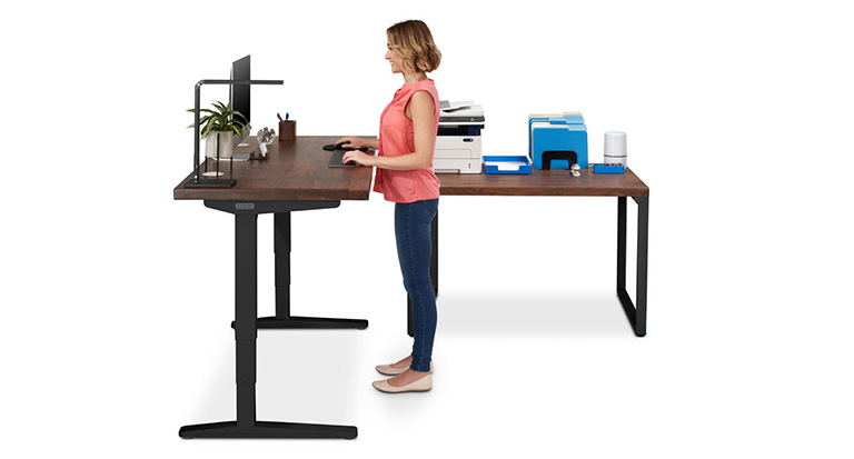 A person standing by an UPLIFT standing Desk and a fixed height UPLIFT table