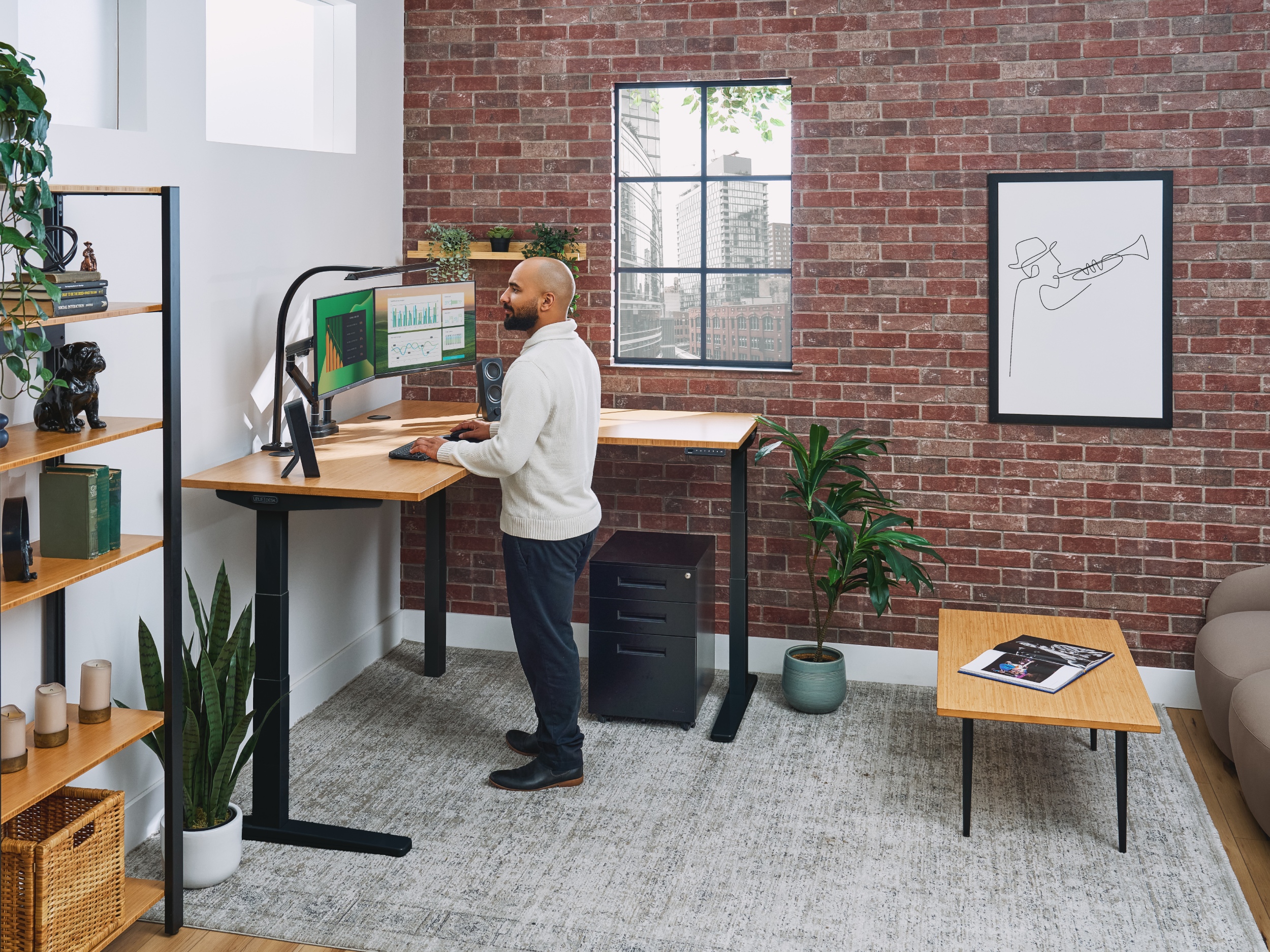 Man standing at a V3 L-shaped standing desk next to a filing cabinet, coffee table, and sequence shelves