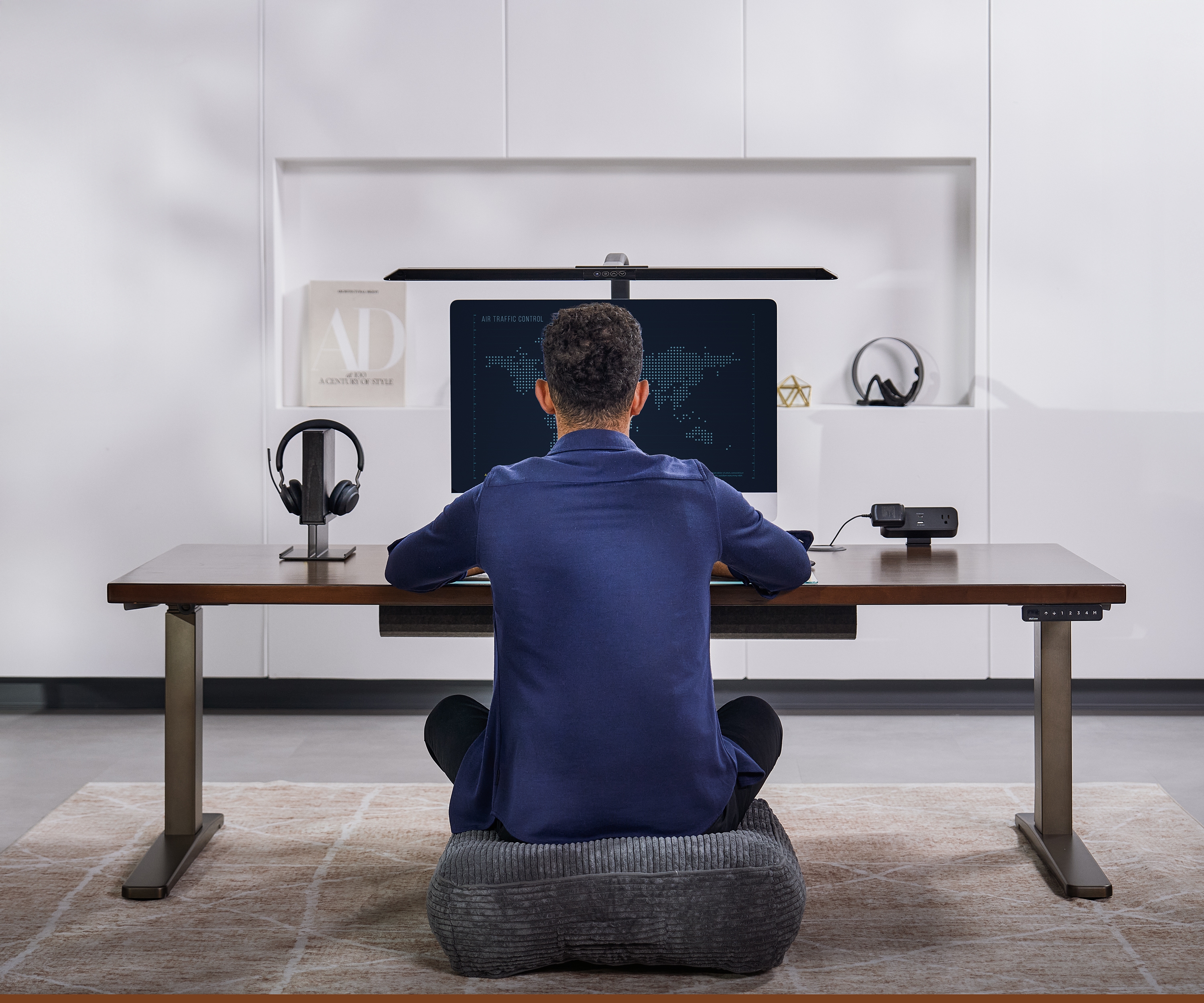 Person sitting on floor cushion working at an Uplift Standing Desk at its lowest height.