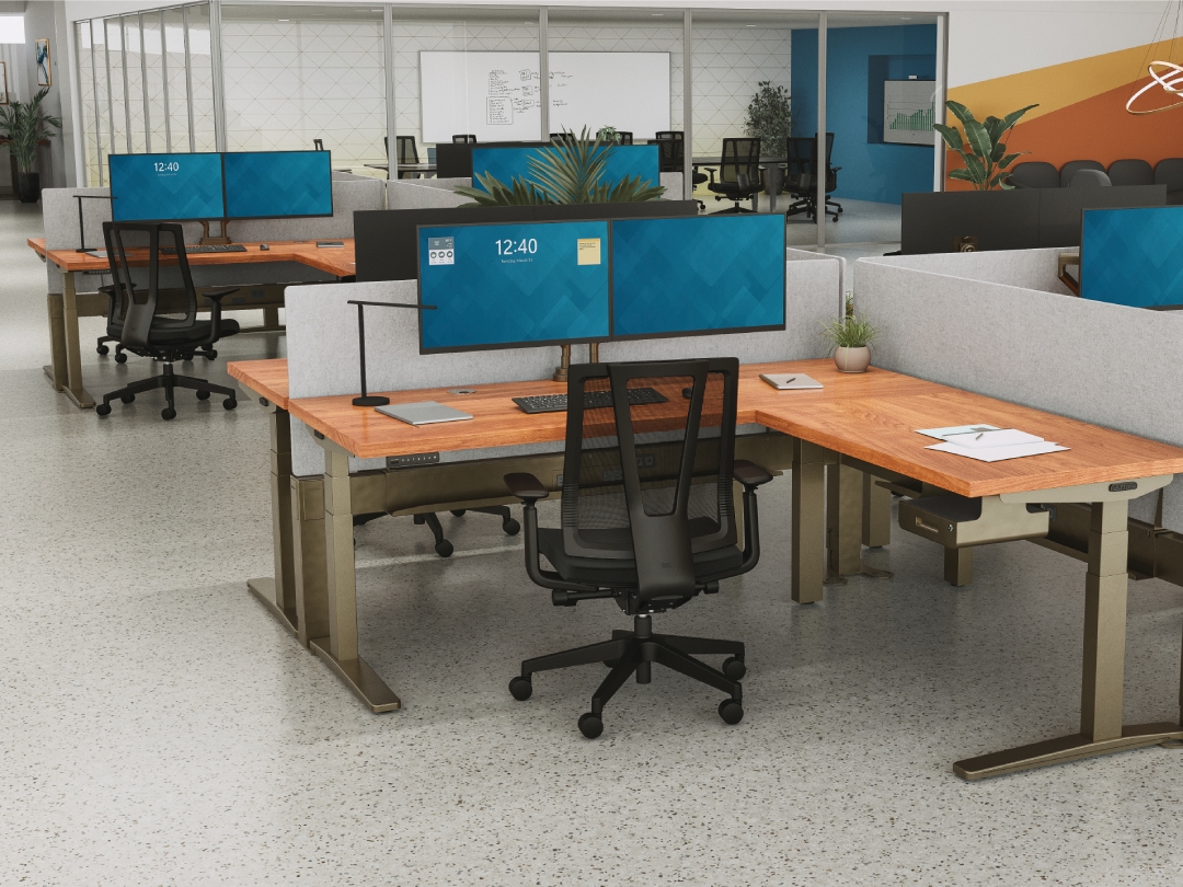 UPLIFT V3 L-Shape standing desk in an open office setting with privacy panels and dual monitor set-up.