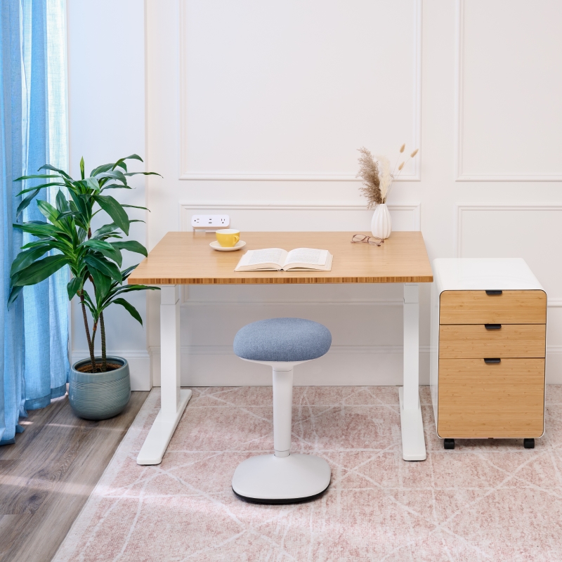UPLIFT Standing Desk with bamboo desktop with an Engage Stool and 3-Drawer File Cabinet in a serene office environment