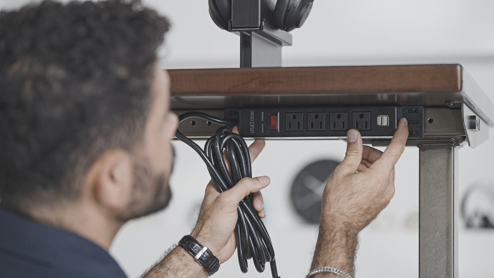 Person installing 4-Outlet Mountable Surge Protector to an Uplift Standing Desk.