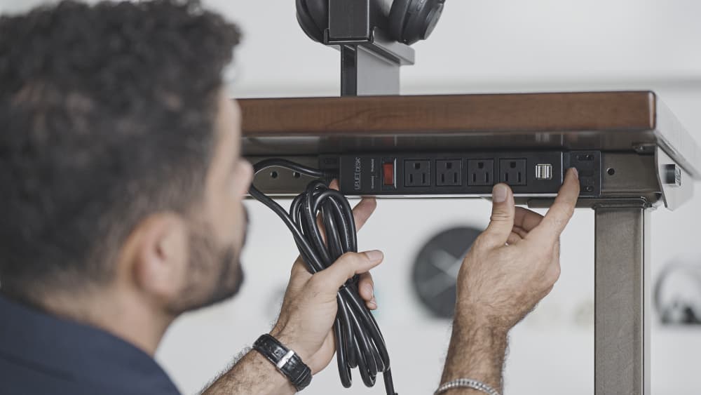 Person installing 4-Outlet Mountable Surge Protector to an Uplift Standing Desk.