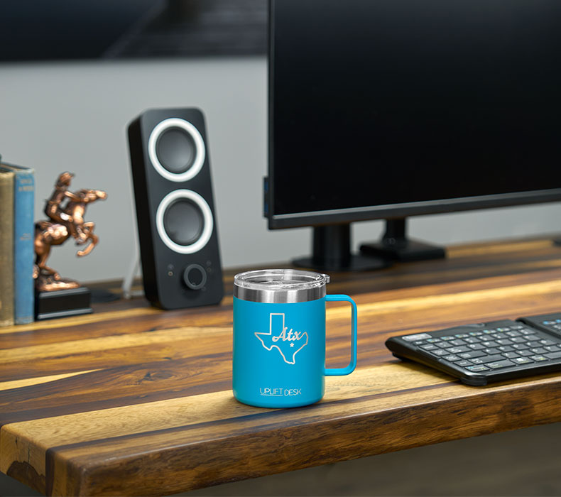 A blue insulated mug on the desktop of an ergonomic sit stand UPLIFT Desk