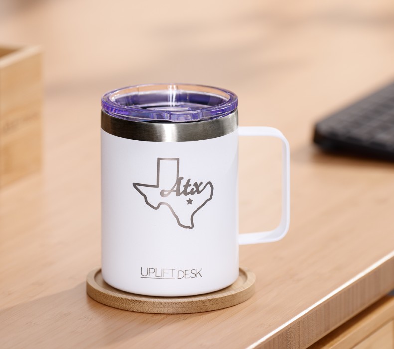A white insulated mug on the desktop of an ergonomic sit stand UPLIFT Desk