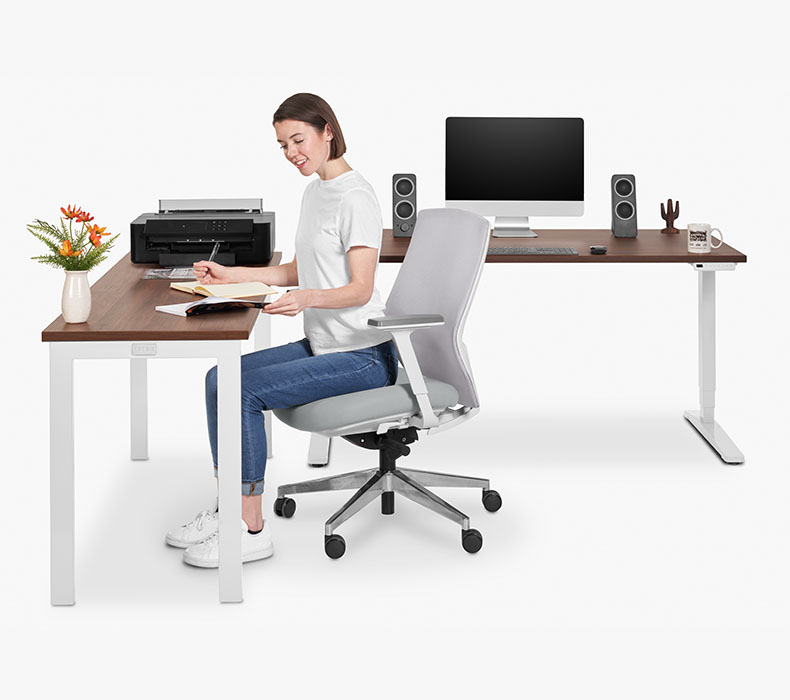 A person working at an UPLIFT Standing desk with a matching Seated Height 4-Leg Small Office Table
