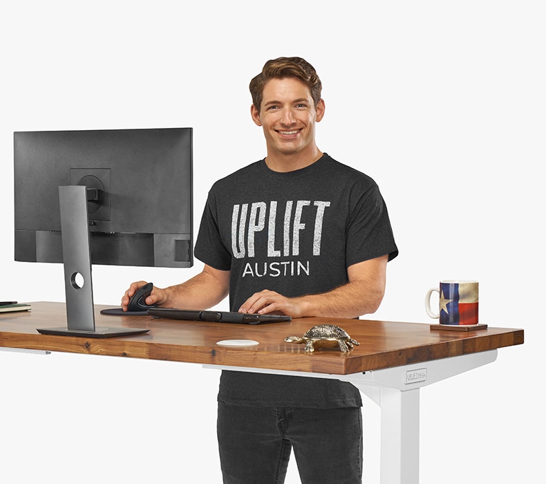 A person wearing a gray Austin Short Sleeve T-Shirt while working at a sit stand UPLIFT Desk