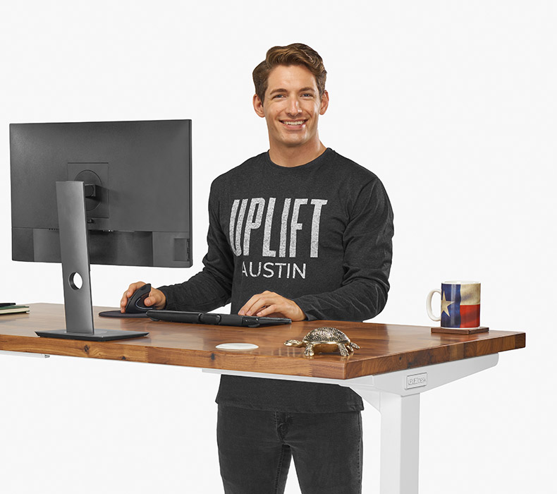A person wearing a gray long sleeve Austin T-Shirt while working at a sit stand UPLIFT Desk