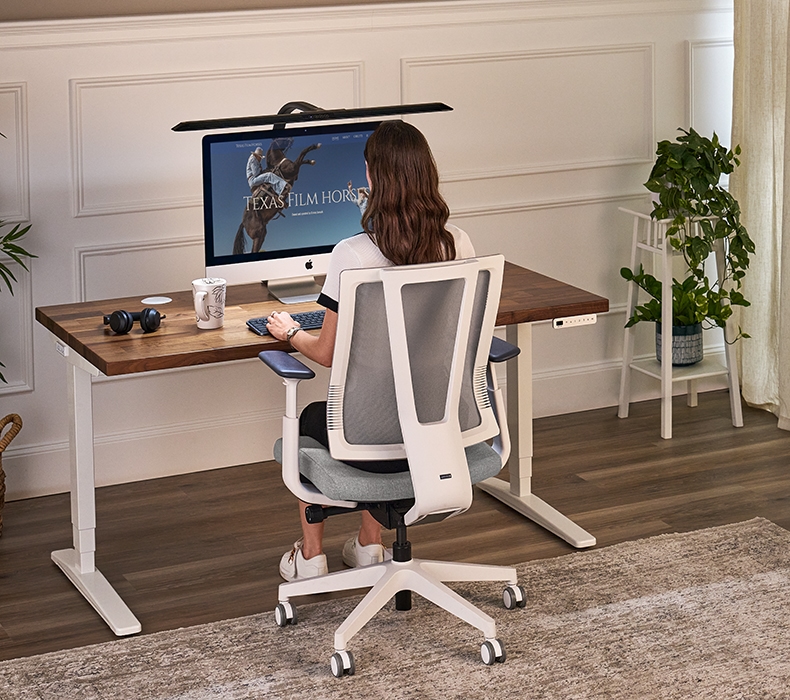 A rear-view of a woman sitting in Clarksville Ergonomic Chair working at an UPLIFT Desk