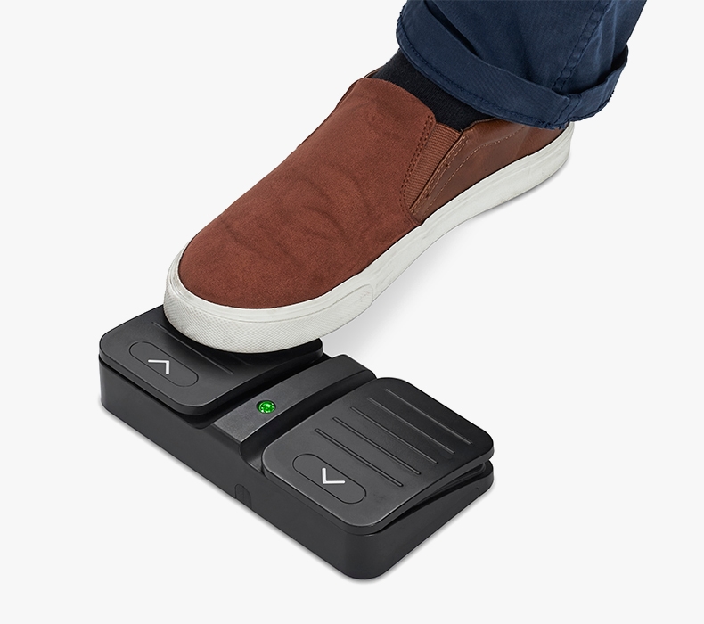 A closeup of a foot stepping on a Wireless Foot Switch in order to lower their UPLIFT Desk.