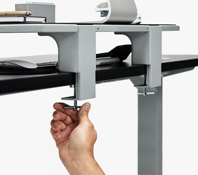 Someone clamping the Desk Shelf to a desktop to add storage to a sit-stand desk