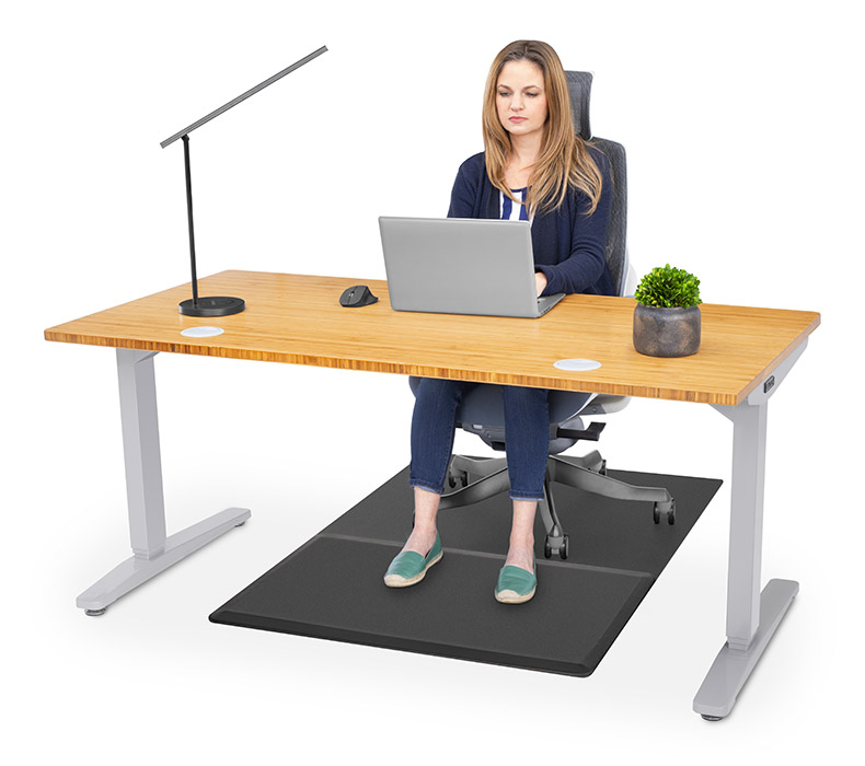 A person working at a Bamboo UPLIFT Sit Stand Desk with their chair and feet on a Chair Mat with Standing Cushion