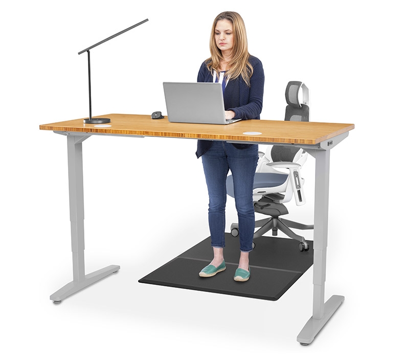 A person standing on a Chair Mat with Standing Cushion while working at a Bamboo UPLIFT Ergonomic Standing Desk
