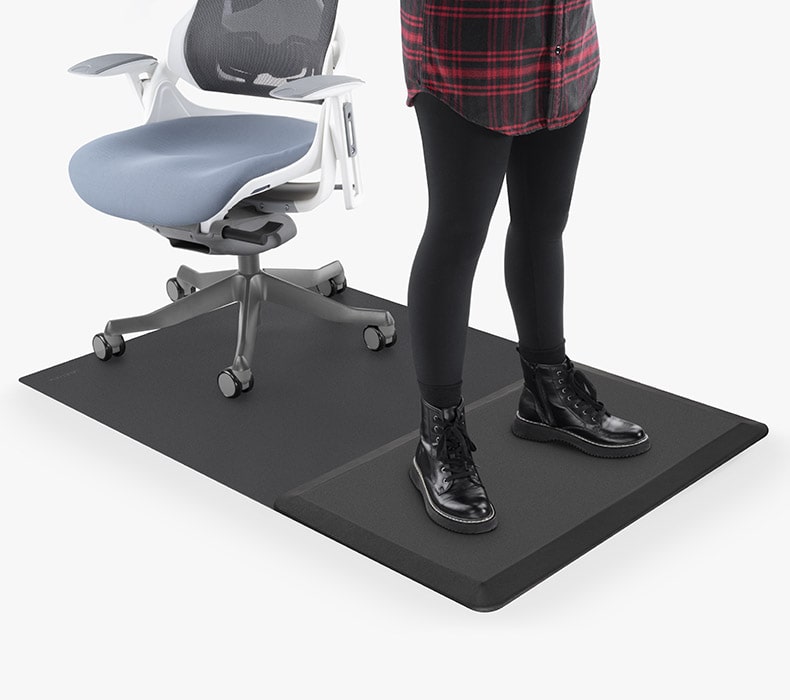 A person standing on the anti-fatigue foam section of the Chair Mat with Standing Cushion with their Pursuit Chair on the rolling portion