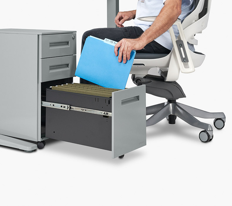 A person places a file in the bottom drawer of an UPLIFT 3-Drawer Narrow Square File Cabinet