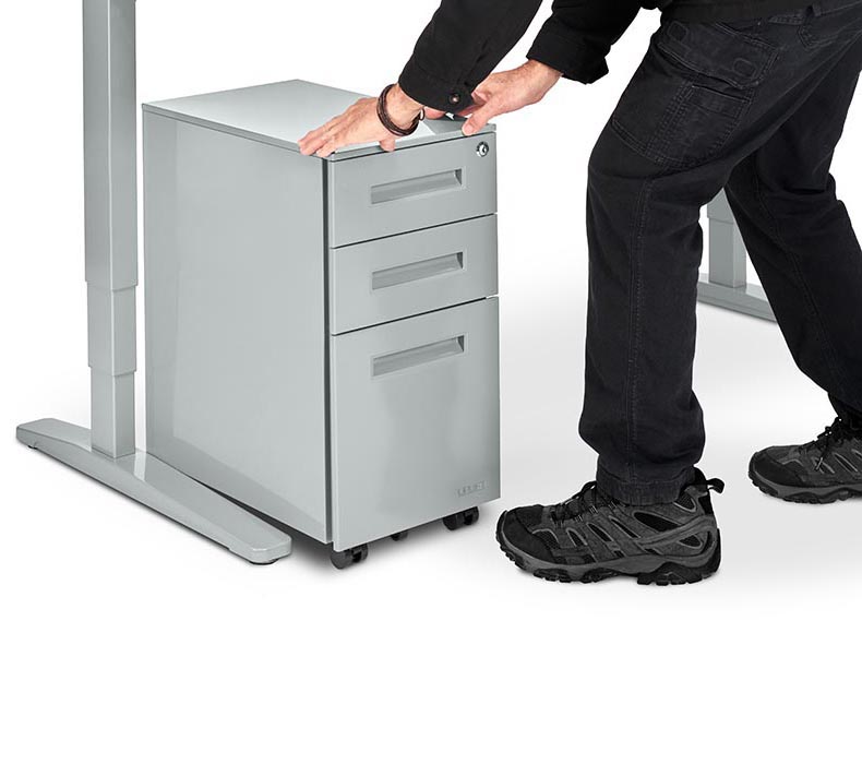 A man rolls a 3-Drawer Narrow Square File Cabinet under an UPLIFT Standing Desk