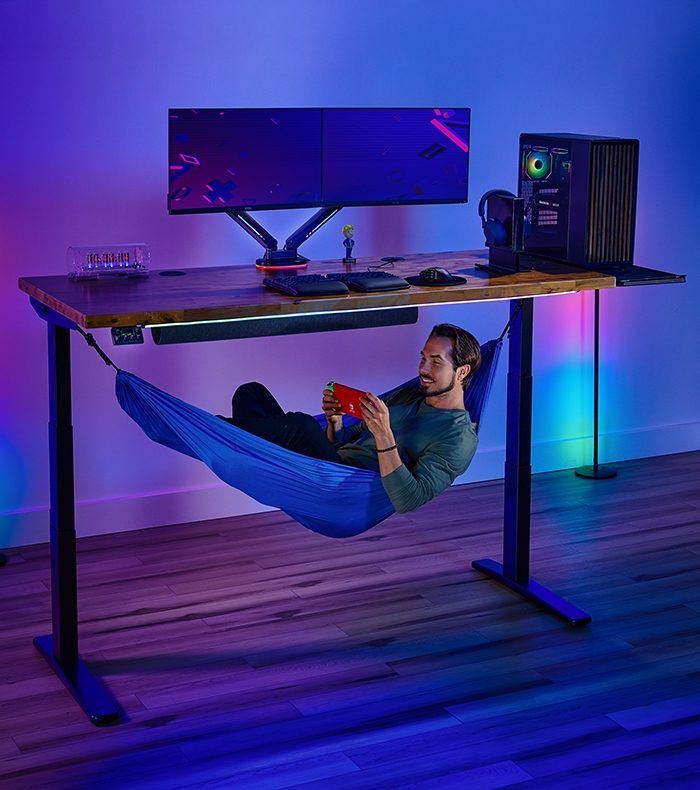 Person relaxing in an Under Desk Hammock attached to an Uplift Standing Desk.