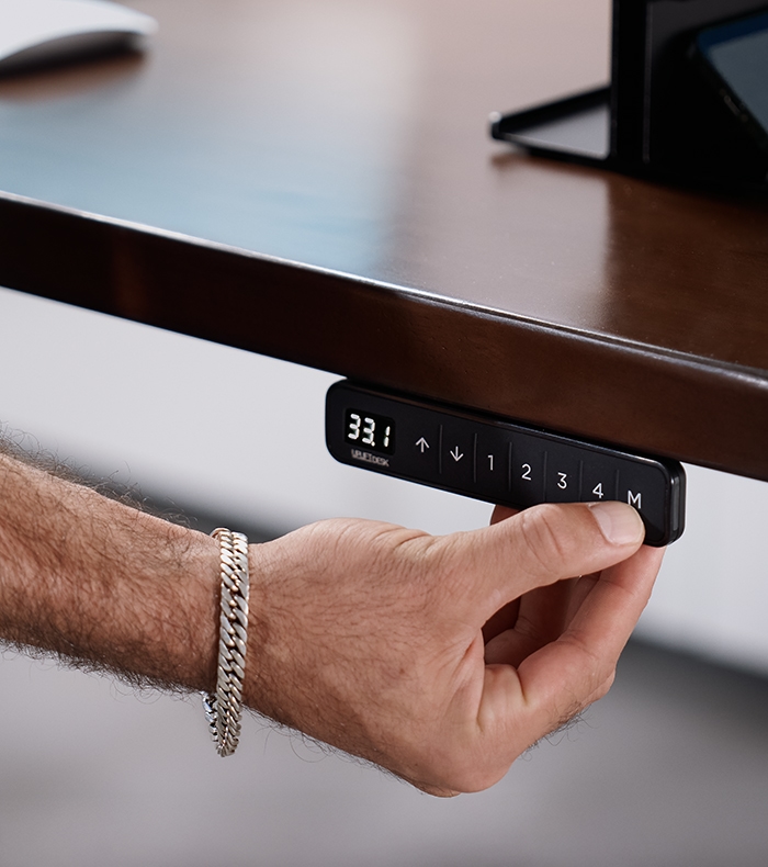 Person pressing a button on the Advanced Keypad attached to an Uplift Standing Desk.
