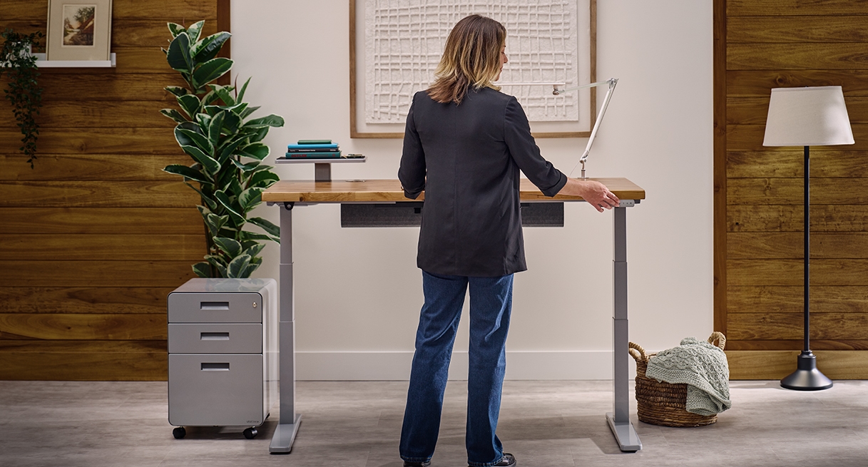 Person standing and pressing a keypad button on an Uplift Standing Desk in Gray with a Reclaimed Birch Butcher Block desktop.