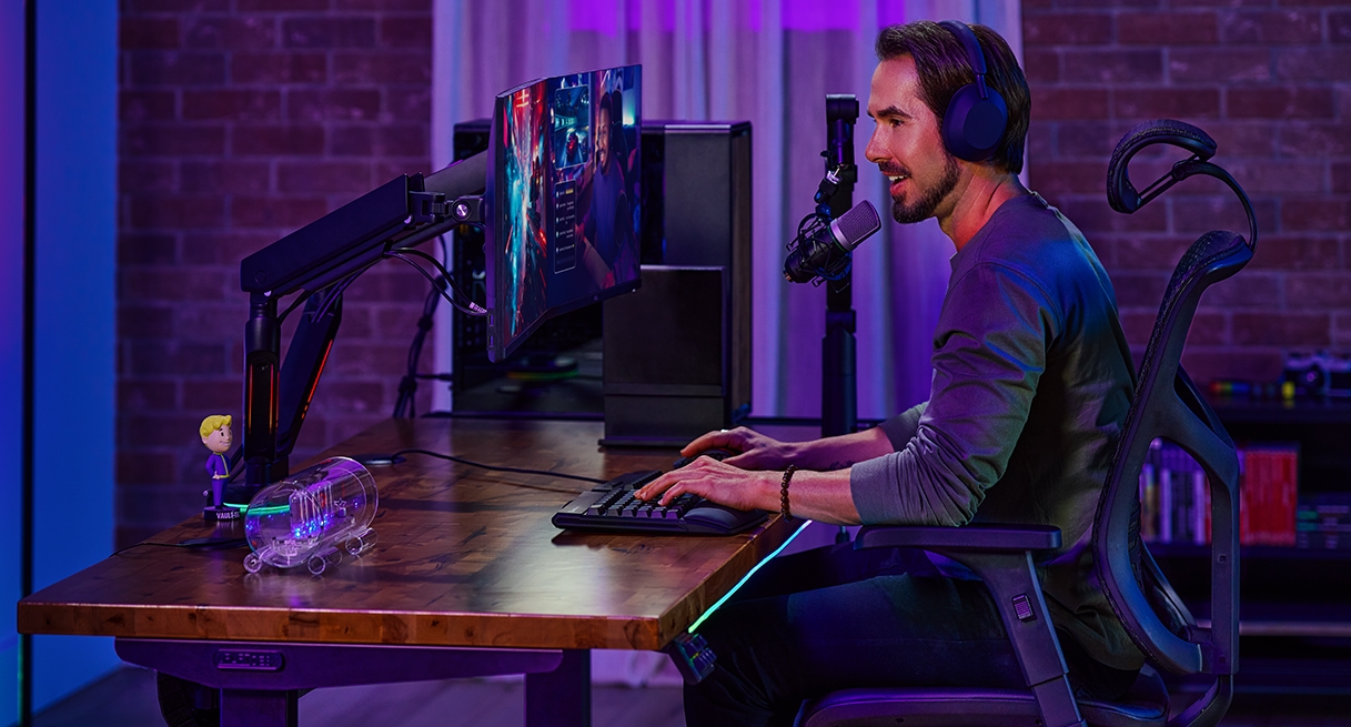 Person sitting and speaking into a microphone at an Uplift Standing Desk in Black with a Saman Butcher Block Desktop.