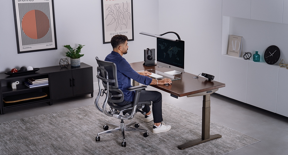 Person sitting and working at an Uplift Standing Desk in Industrial with a Dark Rubberwood Butcher Block desktop.