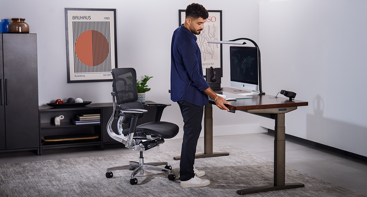 Person pressing keypad button on an Uplift Standing Desk in Industrial with a Dark Rubberwood Butcher Block desktop.