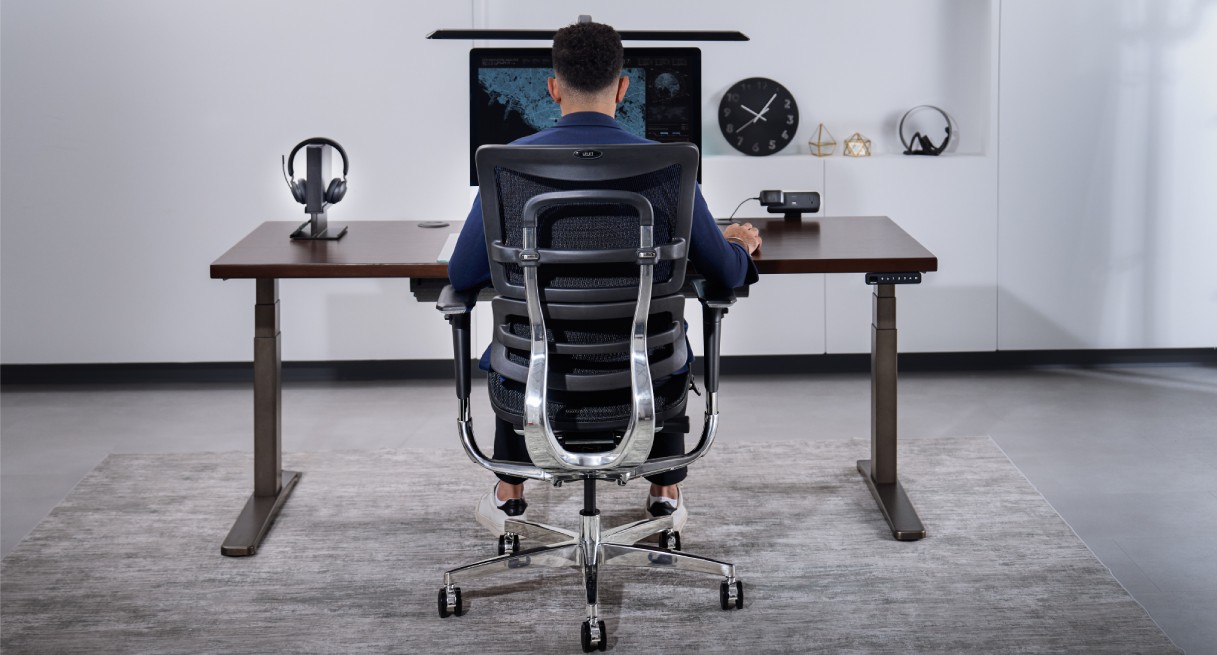 Man working ergonomically at an UPLIFT Desk standing desk, seated in an ergonomic chair in a home office